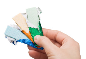 A hand holding 3 different colors of half wrapped gum sticks.